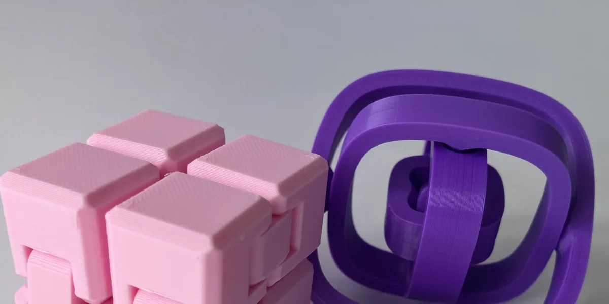 Pink infinity cube next to a purple fidget spinner