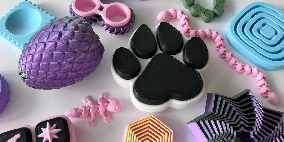 Collection of colourful 3D printed fidget toys including clickers, spinners and articulated toys